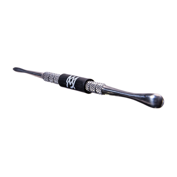 A double-ended metal tool, resembling a dab tool or stylus, lies against a light background. It features textured grips and a central black band with a white "MJ" logo.