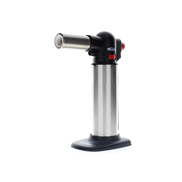 A silver culinary blowtorch stands upright with a black handle and red ignition button, set against a plain black background.